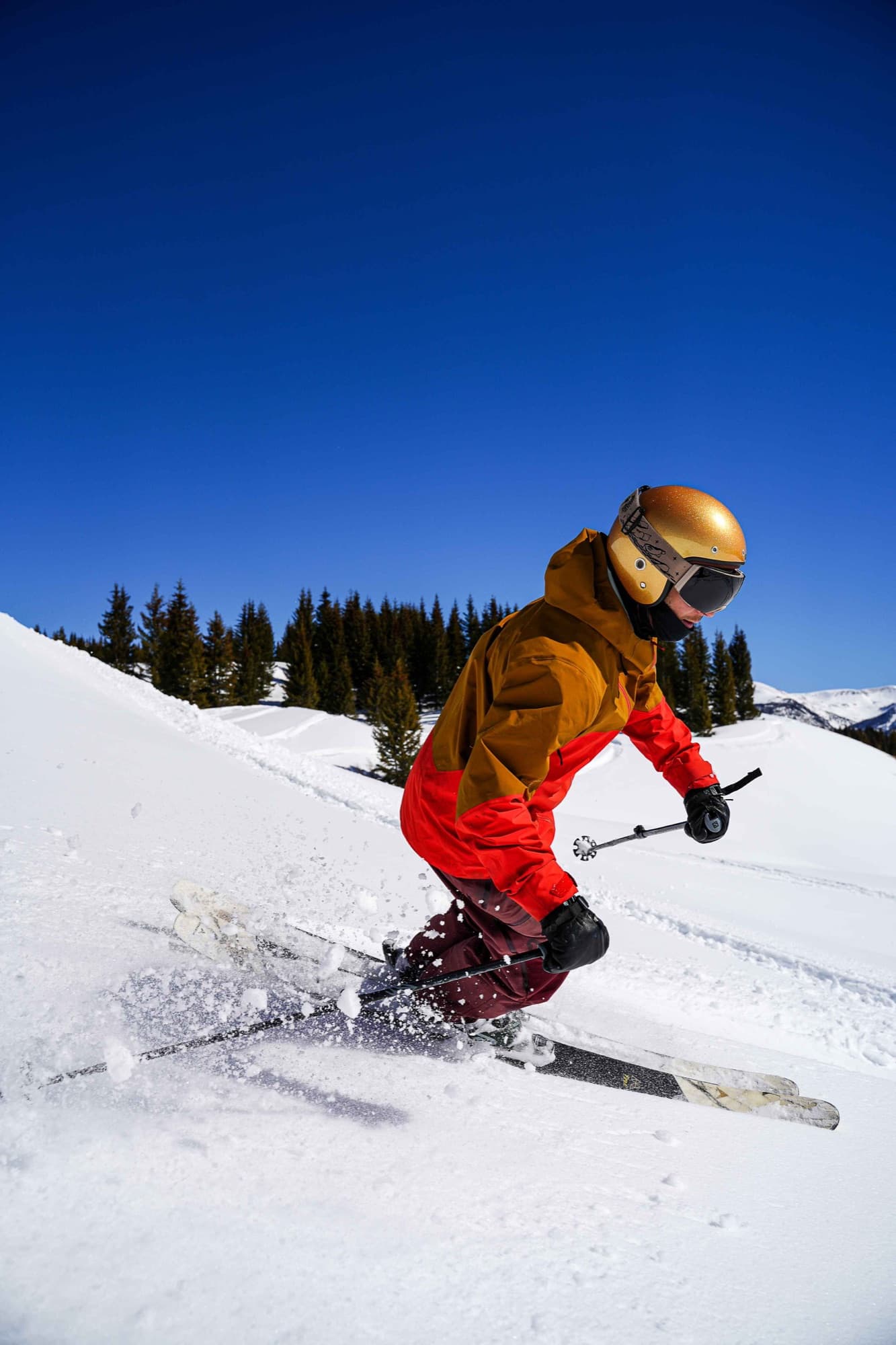 A skier in a gold Lowdown helmet carves through fresh snow