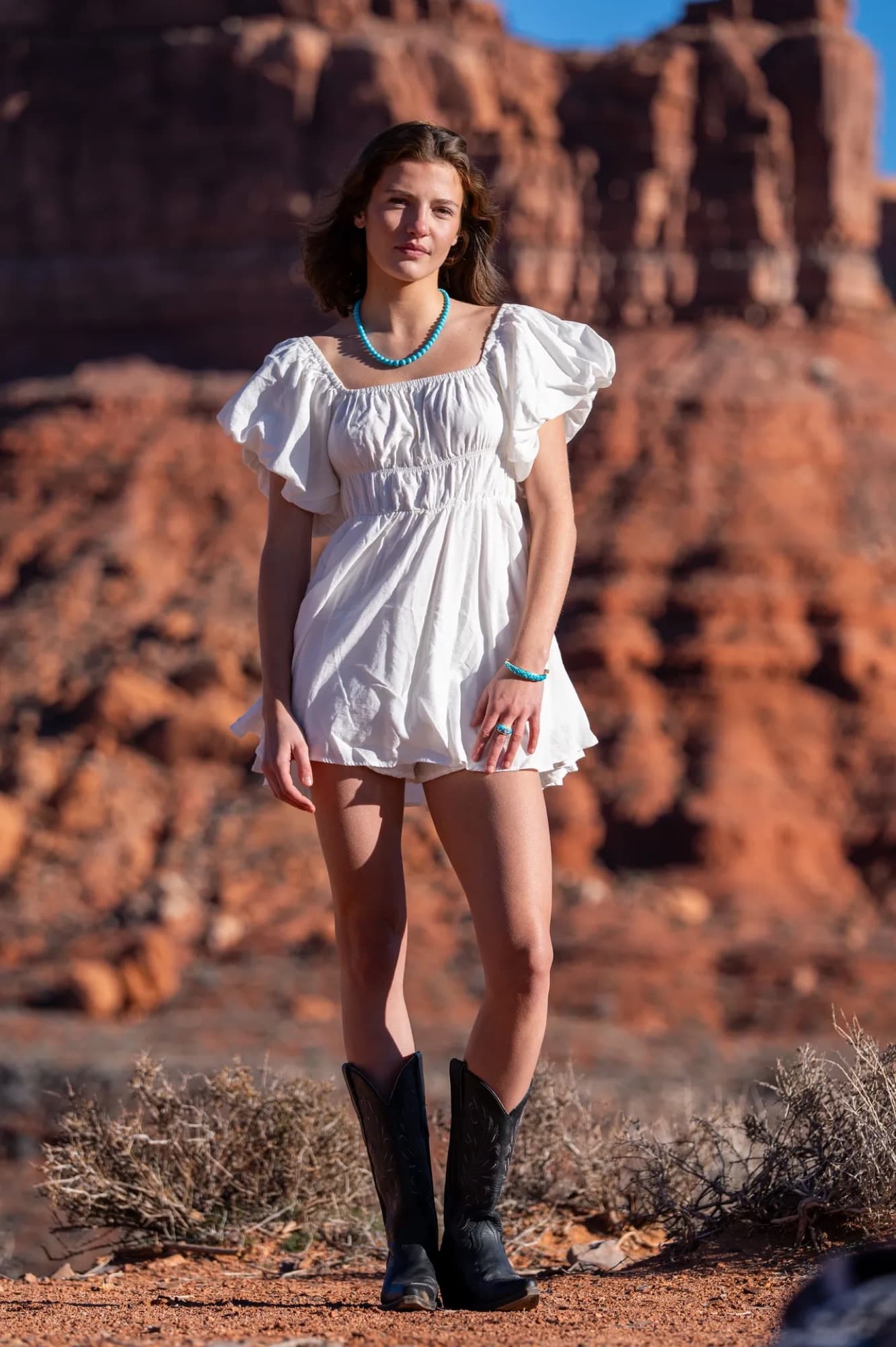 A model in a white dress and boots photographed against red sandstone