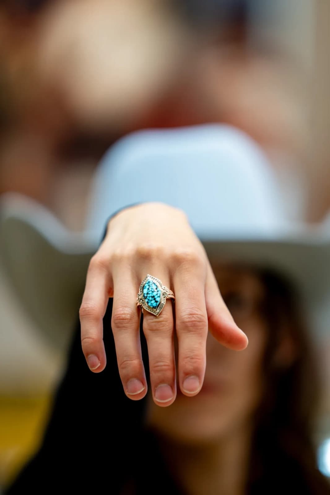 A hand wearing a turquoise ring, a hat brim soft in the foreground