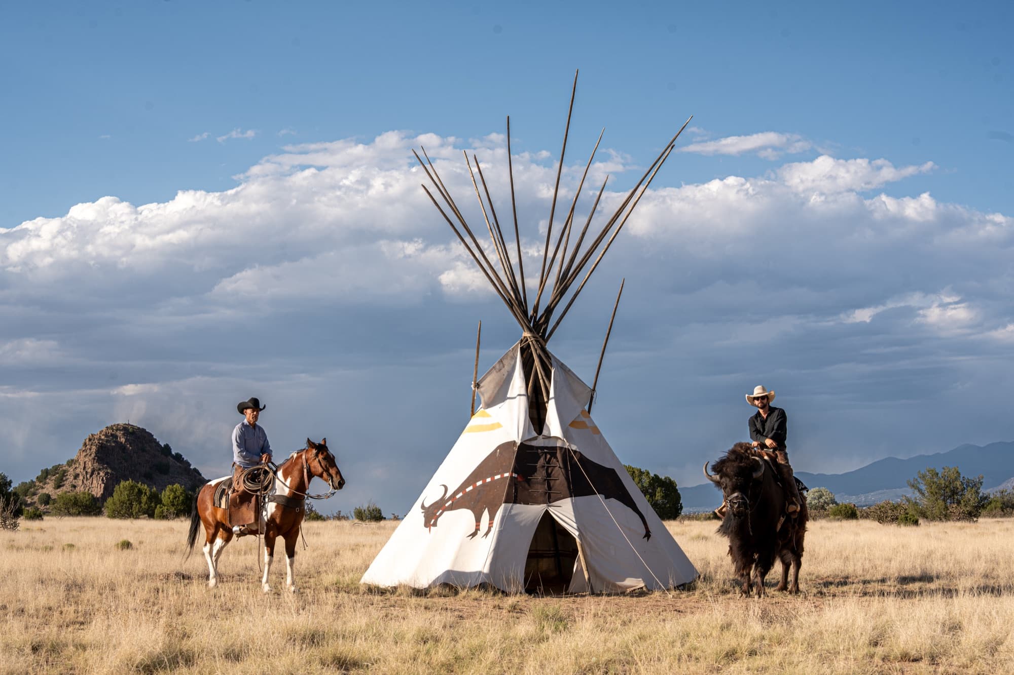 A teepee on the ranch grounds with riders in the distance